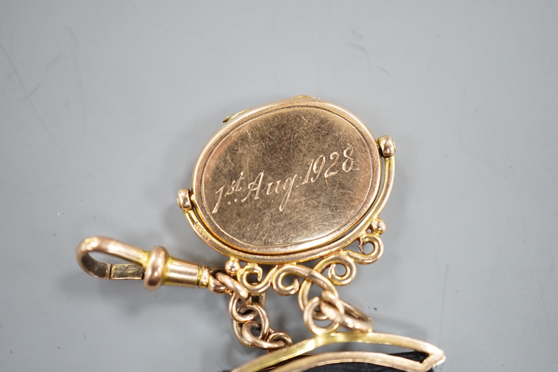 A Victorian yellow metal oval locket fob, hung from a yellow metal mounted black suspension sash, with later engraved date and initials.